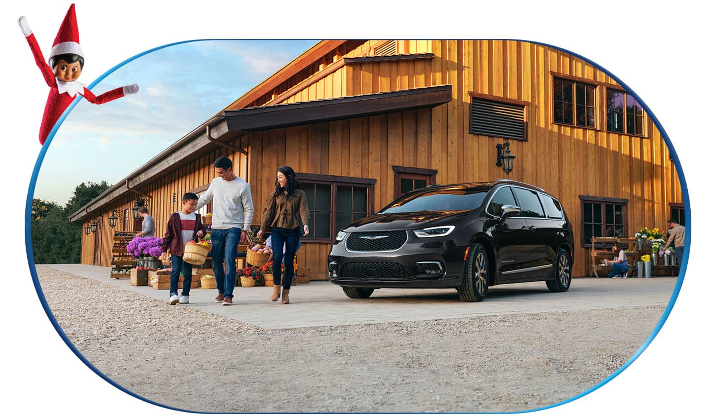 A mom, dad and son carrying baskets of produce near a black 2026 Chrysler Pacifica Pinnacle Plug-in Hybrid at a farmers market, as Sparkles, the Elf on the Shelf looks on from the upper left corner of the image.
