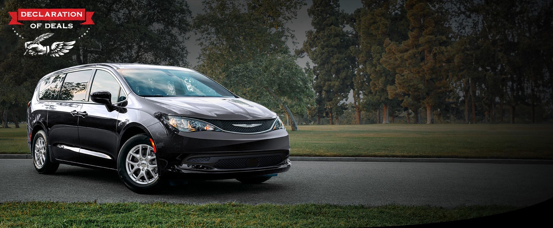 A front passengers side view of a black 2026 Chrysler Voyager LX in a parking lot of a park. Declaration of Deals Sales Event.
