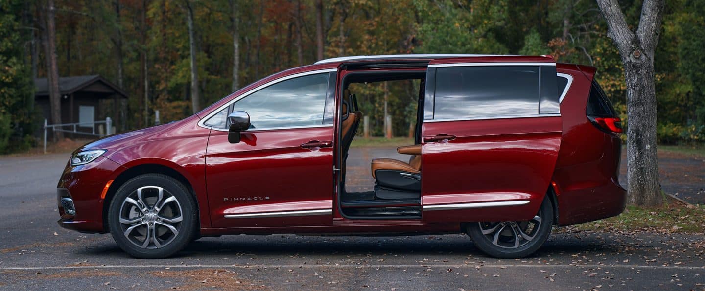 Toma de perfil del lado del conductor de una Chrysler Pacifica Pinnacle 2025 roja con sus dos puertas eléctricas laterales corredizas abiertas.