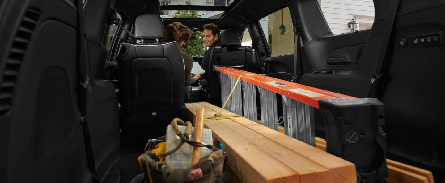 El interior de la Chrysler Pacifica 2025 con la tercera fila y uno de los asientos Stow n Go de la segunda fila plegados hacia el piso, con el fin de acomodar una escalera y piezas largas de madera.