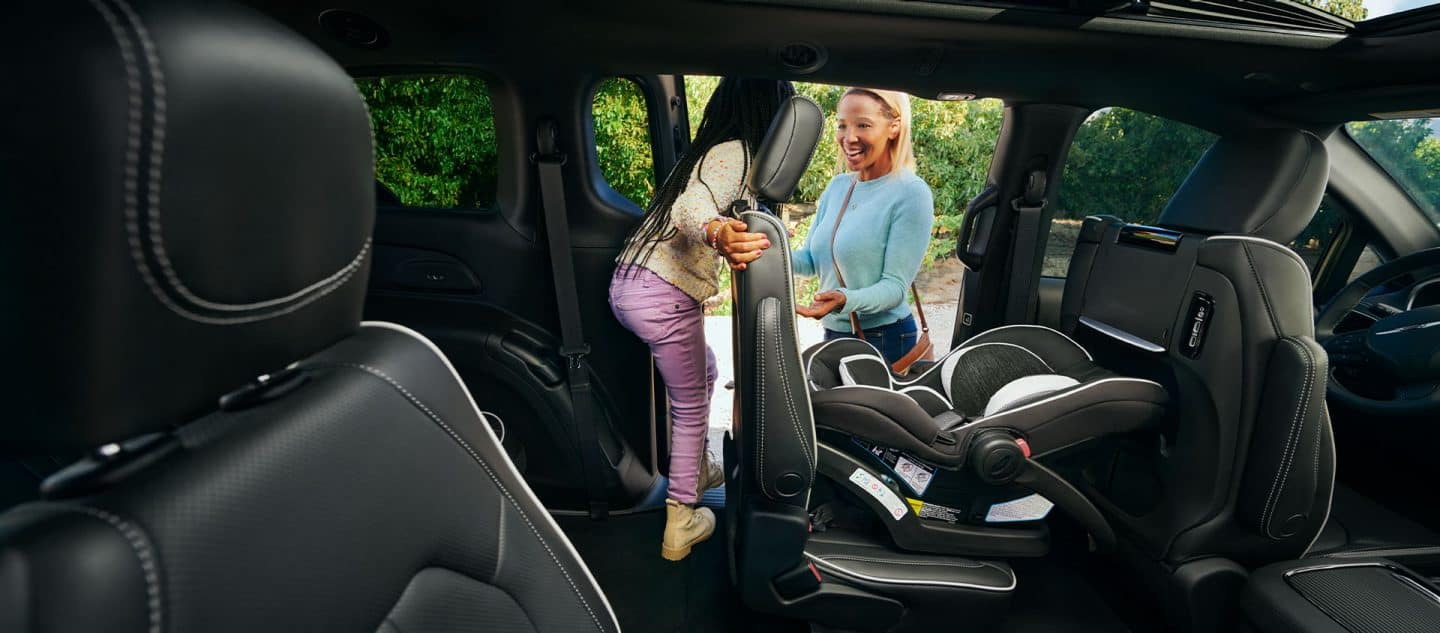 El interior de la Chrysler Pacifica Select Hybrid 2025 enchufable con el paquete de apariencia Premium S, el asiento de la segunda fila inclinado hacia adelante mientras sale una niña de la tercera fila a través de la puerta corrediza del lado del conductor.