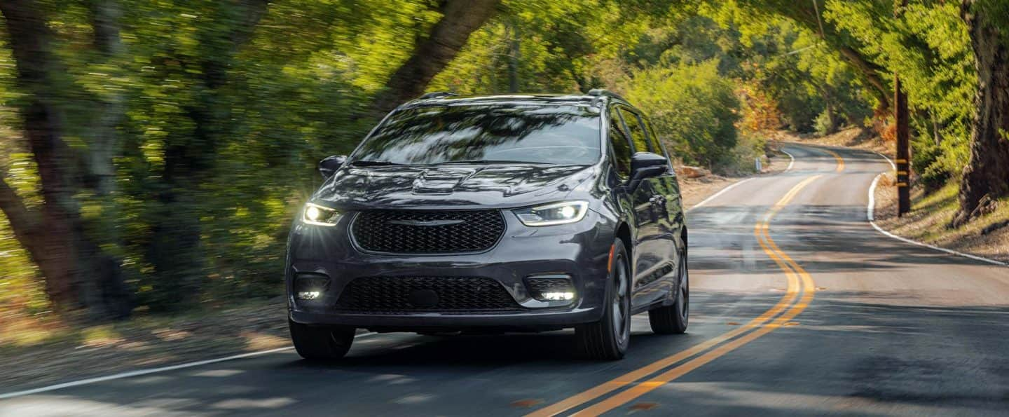 Una Chrysler Pacifica Limited 2025 gris circulando por una carretera sinuosa en el bosque.