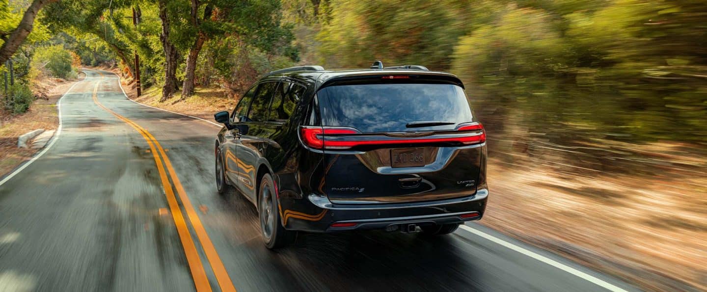 Ángulo trasero de una Chrysler Pacifica Limited 2025 negra circulando por un camino rural. El fondo está borroso para indicar que el vehículo está en movimiento.