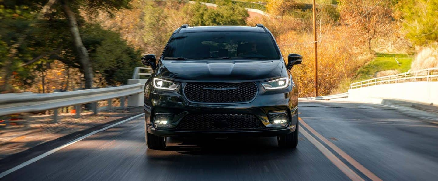 Ángulo delantero de una Chrysler Pacifica Limited 2025 negra circulando por una carretera. El fondo está borroso para indicar que el vehículo está en movimiento.