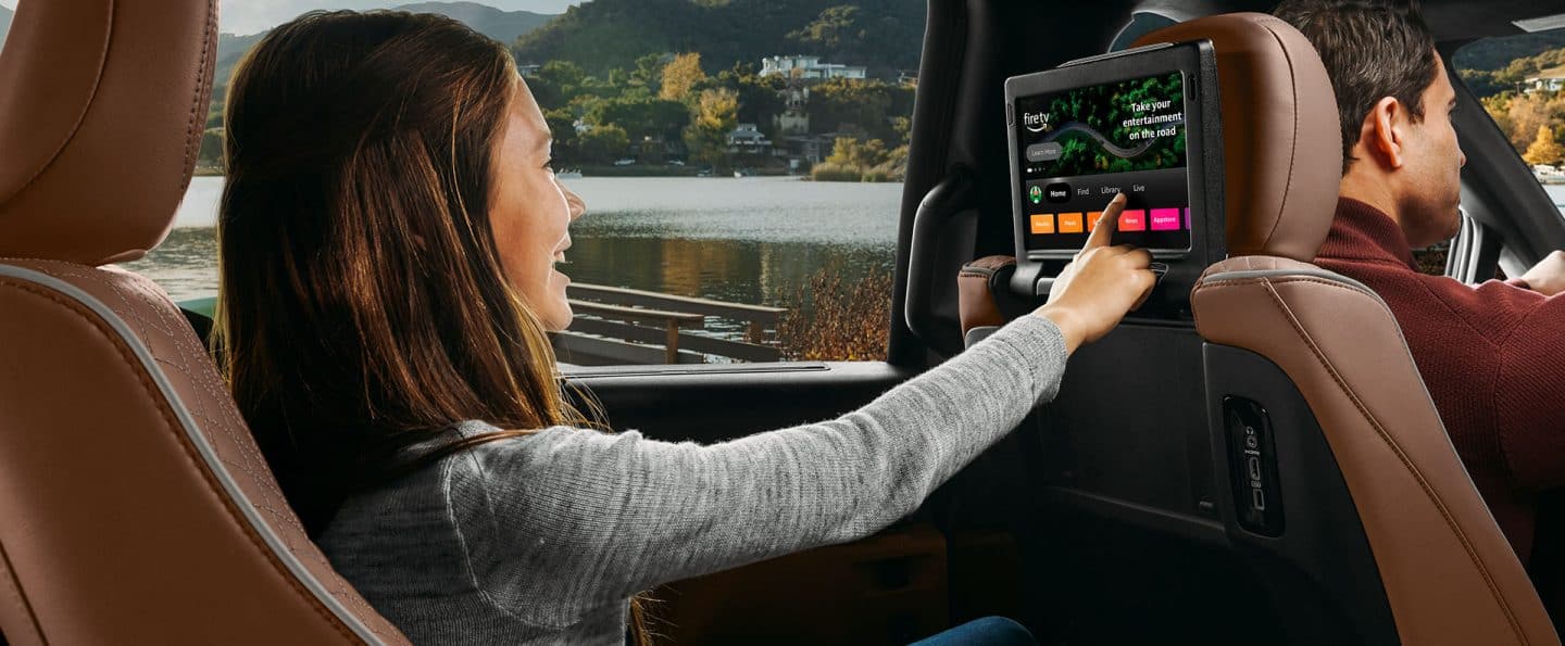 Una joven en el asiento de la segunda fila del lado del conductor de la Chrysler Pacifica Pinnacle 2025 haciendo una selección en la pantalla táctil montada en el respaldo del asiento delantero, en la que se muestra Amazon FireTV.