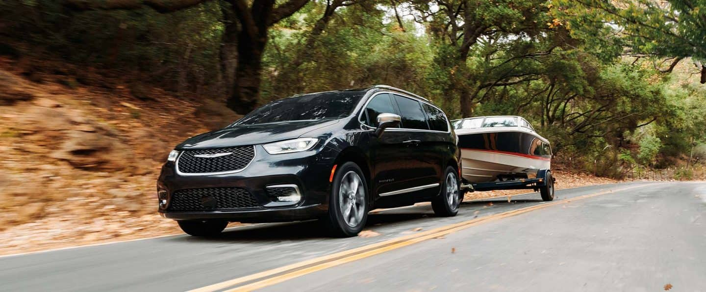 Una Chrysler Pacifica Pinnacle 2025 negra circulando por una carretera, remolcando una lancha. El fondo está borroso para indicar que el vehículo está en movimiento.