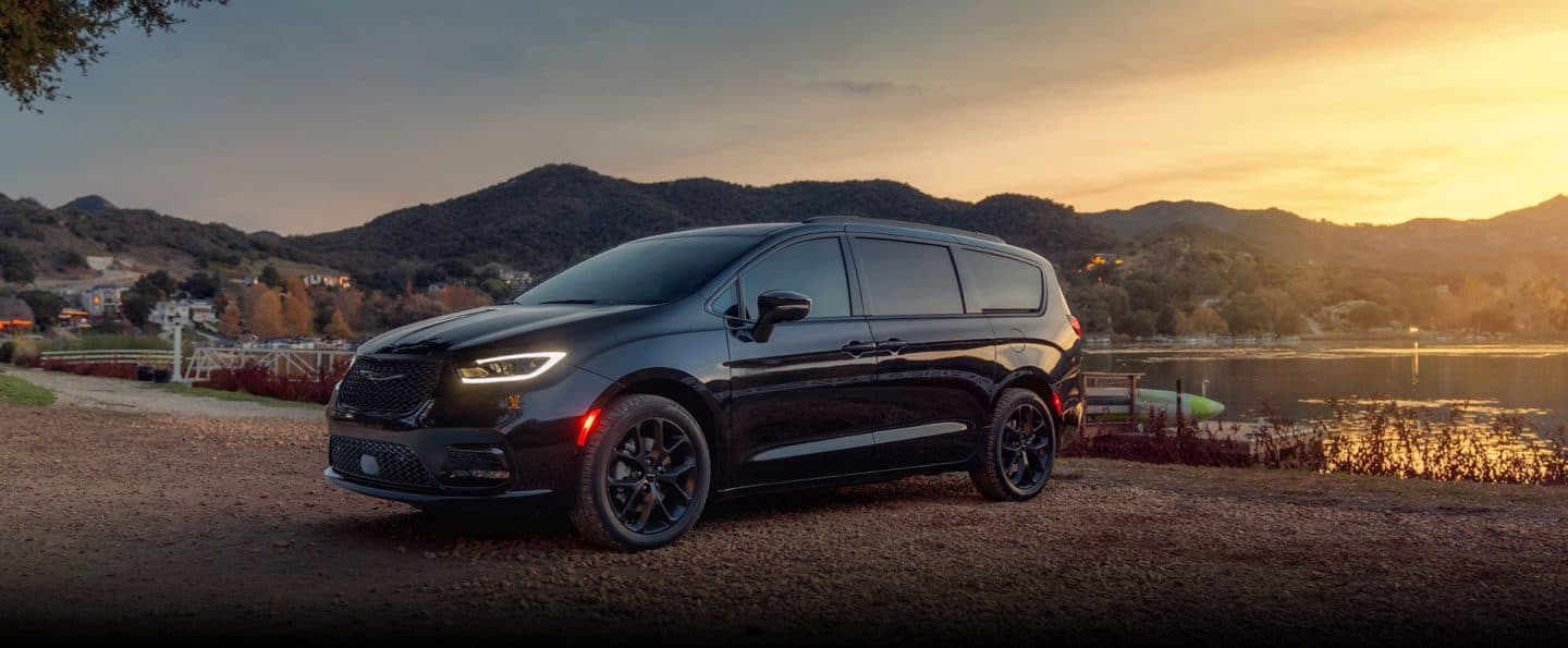 Una Chrysler Pacifica Limited 2025 negra estacionada al lado de un lago, al atardecer.