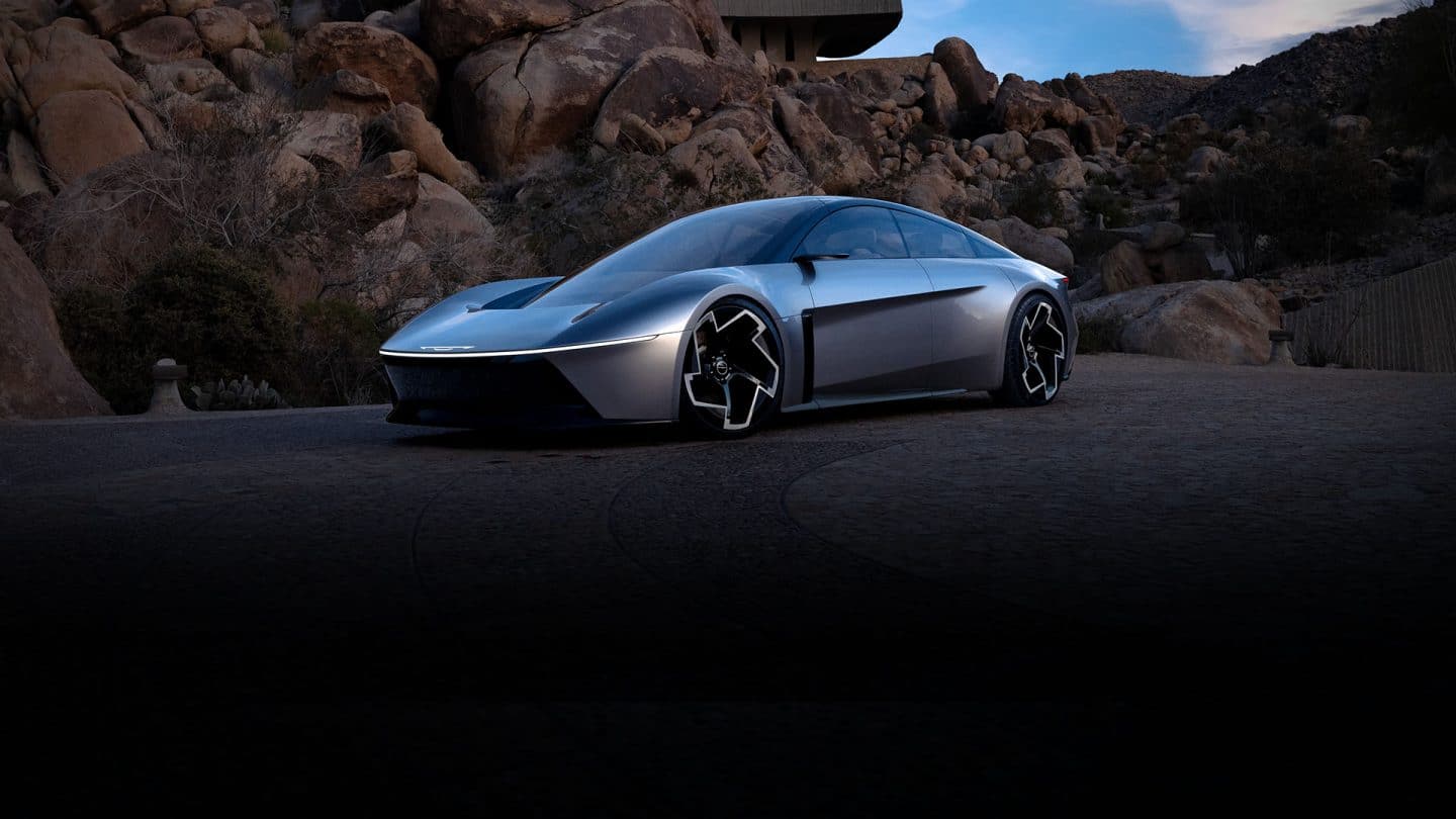 A front driver-side angle of the silver Chrysler Halcyon Concept vehicle parked on a clearing with rock formations in the background.