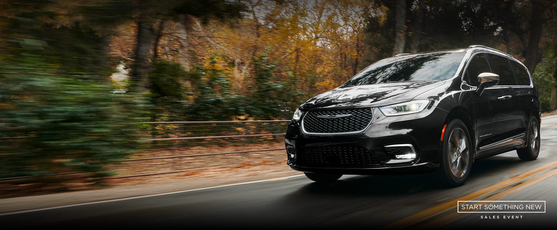 An angled driver-side profile of the 2024 Chrysler Pacifica Pinnacle being driven down a country road, the background is blurred to indicate the vehicle is in motion. Start Something New sales event. 