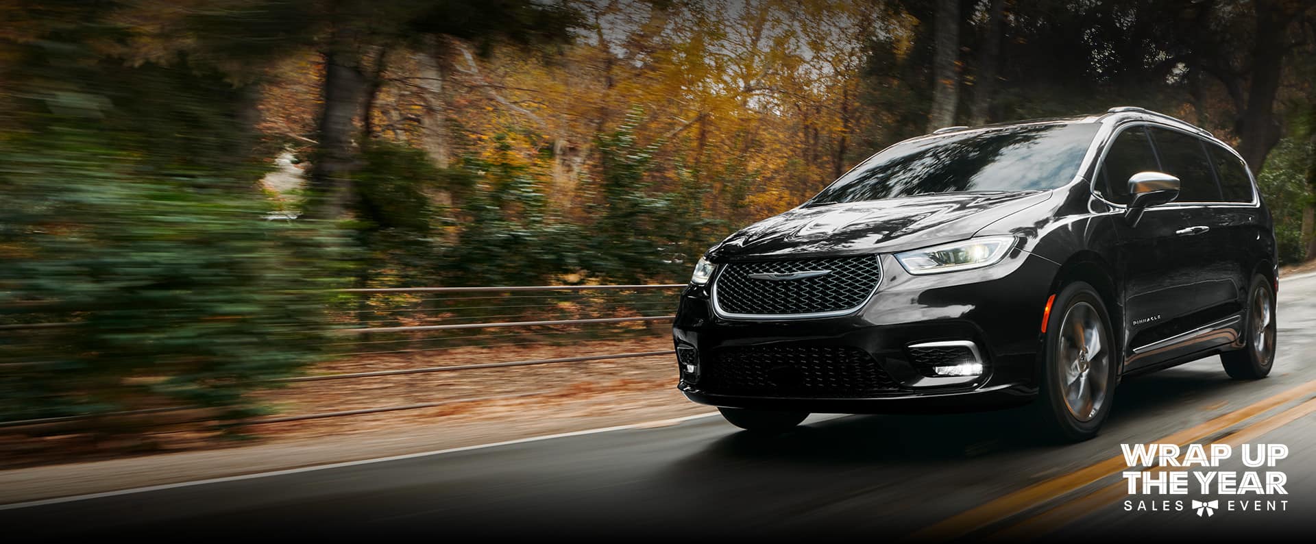 An angled driver-side profile of the 2024 Chrysler Pacifica Pinnacle being driven down a country road, the background is blurred to indicate the vehicle is in motion. Wrap up the Year sales event.