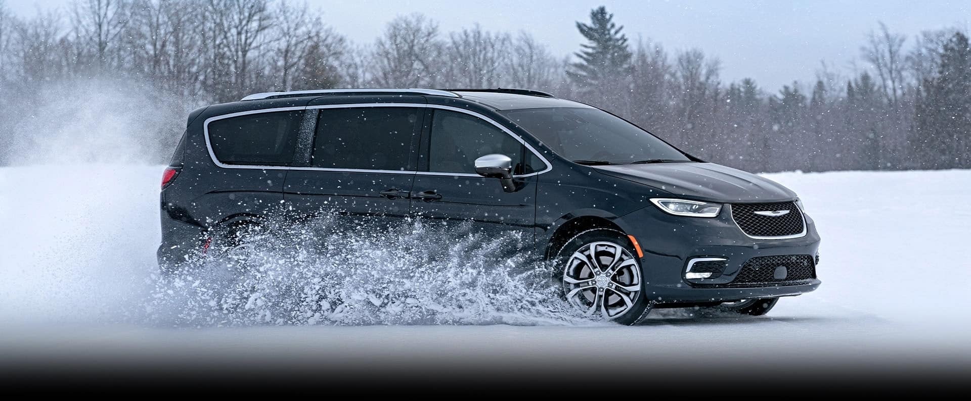 A black 2025 Chrysler Pacifica Pinnacle traveling on a snow-covered road in the woods.