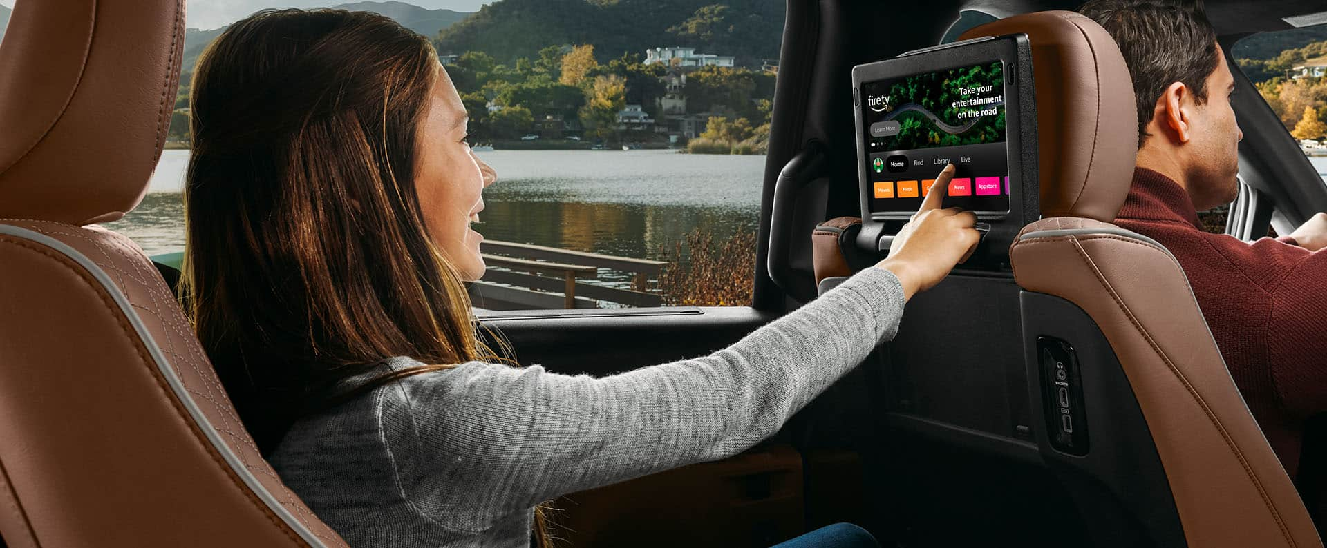 A young girl in the driver-side second-row seat of the 2025 Chrysler Pacifica Pinnacle making a selection on the front seatback-mounted touchscreen that is displaying Amazon FireTV.