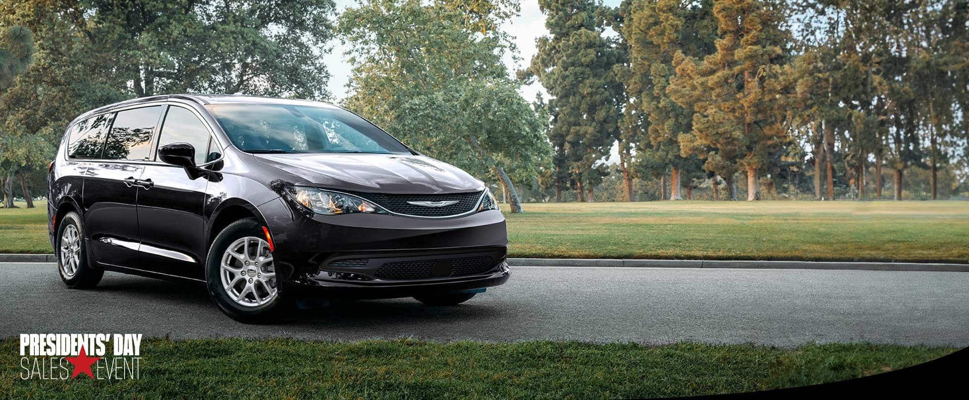 A front pasengers side view of a black 2025 Chrysler Voyager LX in a parking lot of a park. Presidents' Day sales event. 