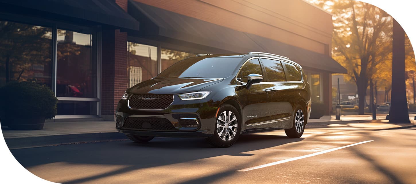 A black 2026 Chrysler Pacifica Plug-in Hybrid Pinnacle parked in front of a block of shops.