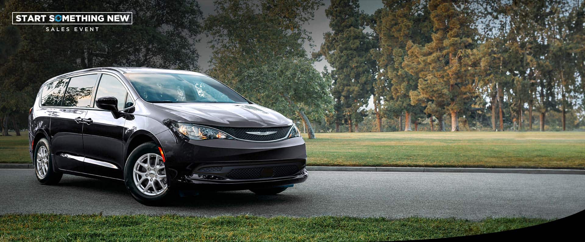 A front passengers side view of a black 2026 Chrysler Voyager LX in a parking lot of a park. Start Something New Sales Event.