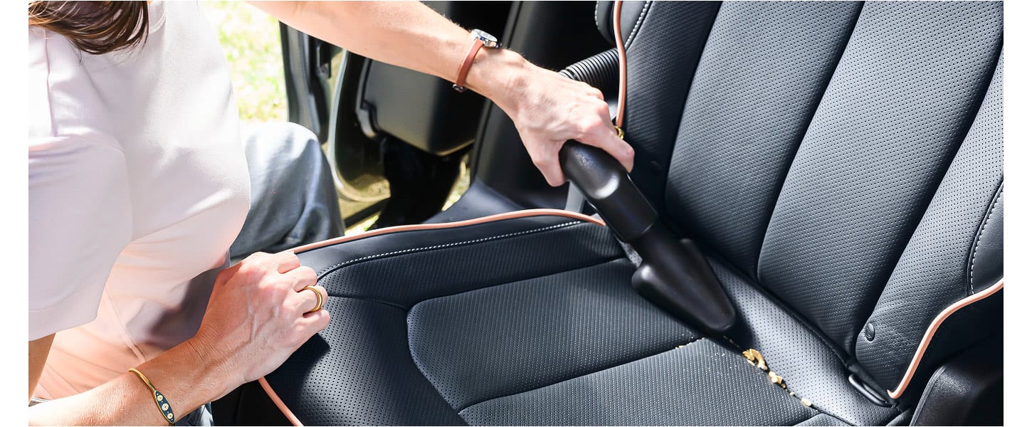 A close up of a woman standing at the open sliding side door of the 2027 Chrysler Pacifica, vacuuming the second-row carpeting with the integrated vacuum.