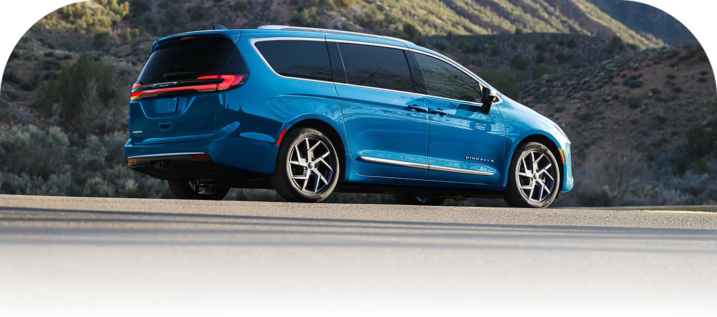 A passenger-side rear angle of a blue 2027 Chrysler Pacifica Pinnacle on a mountain road.