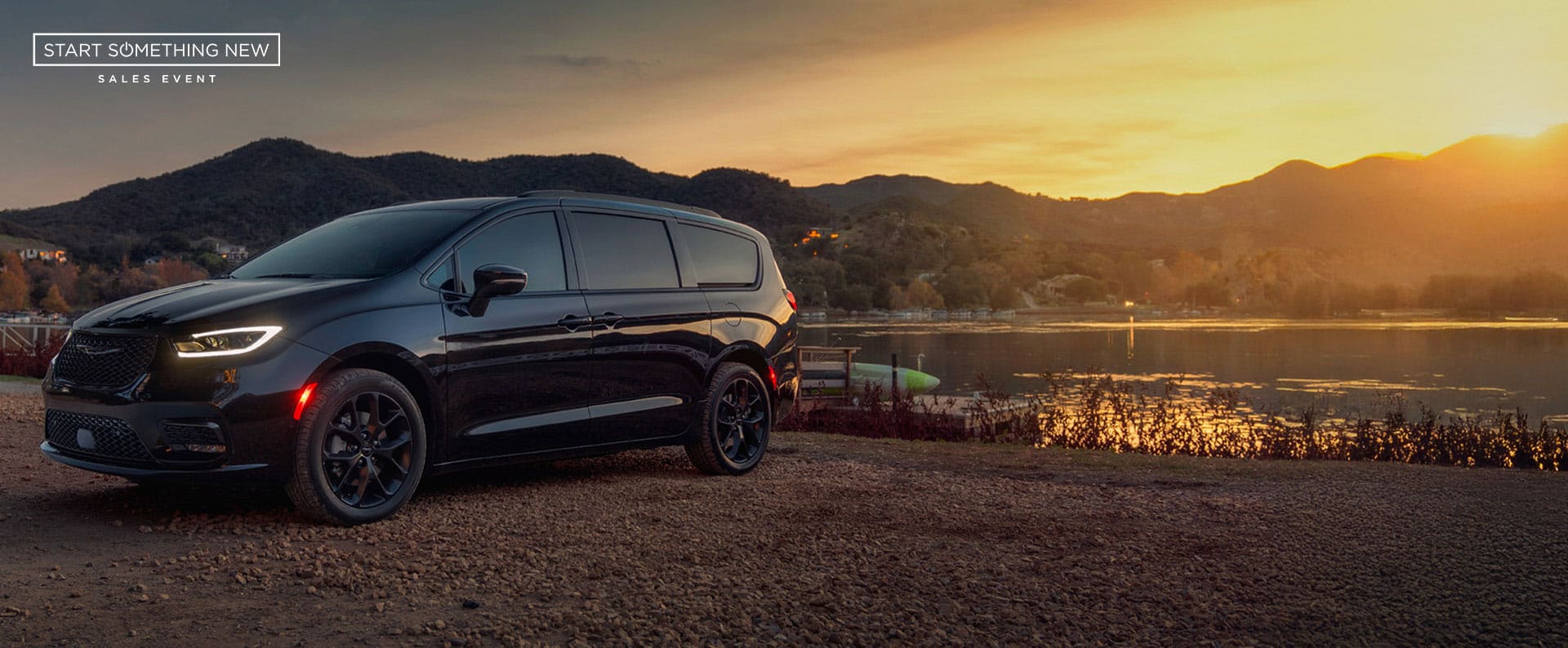 A black 2025 Chrysler Pacifica Limited parked by a lake at sunset. Start Something New sales event.