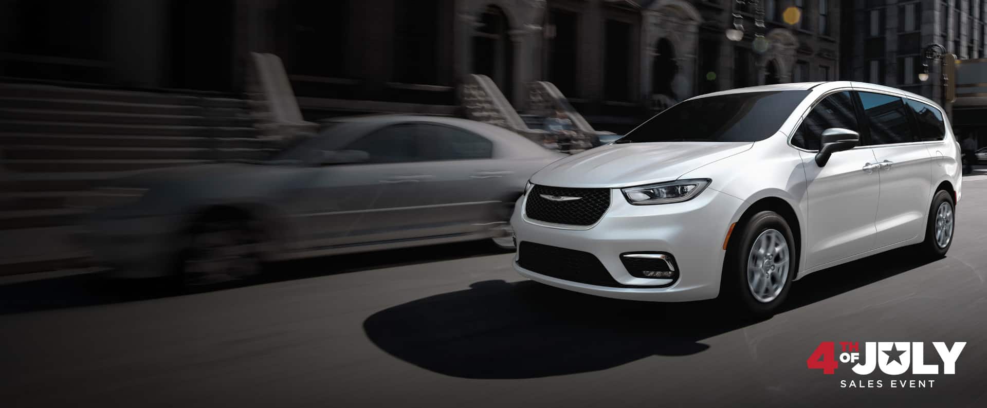 A white 2026 Chrysler Pacifica Select driving down a city street. 4th of July Sales Event.