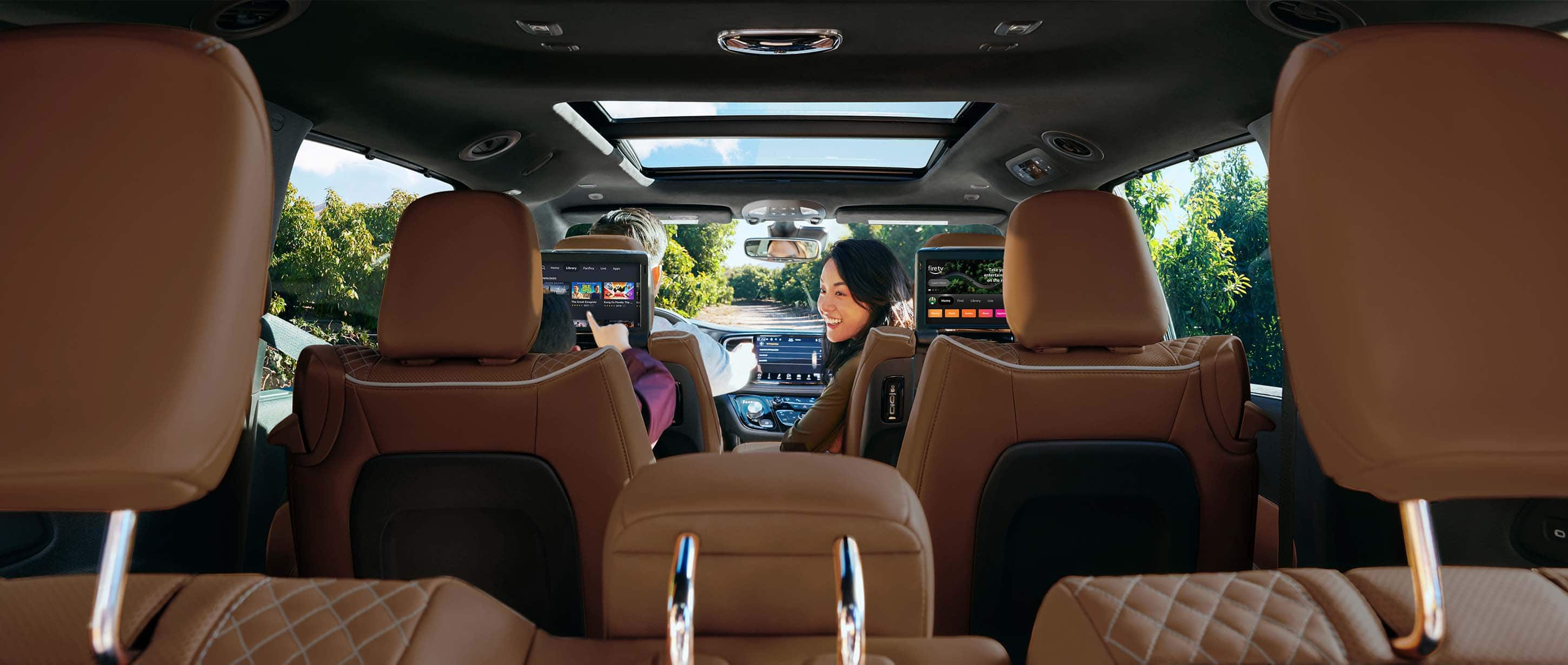 The interior of the 2024 Chrysler Pacifica from behind the third-row seats, with children in the second row making selections on the touchscreens mounted to the back of the front seats.